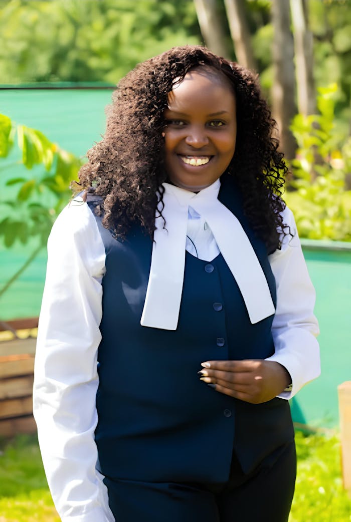 Smiling professional woman in business formal attire outdoors with green surroundings.